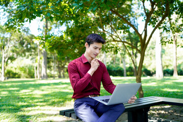 Young man working on laptop outdoors in a sunny park setting while enjoying a vibrant and professional lifestyle