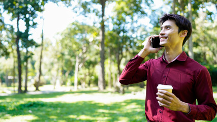 Young asian man with takeout coffee communicating on smartphone at urban park, blank space