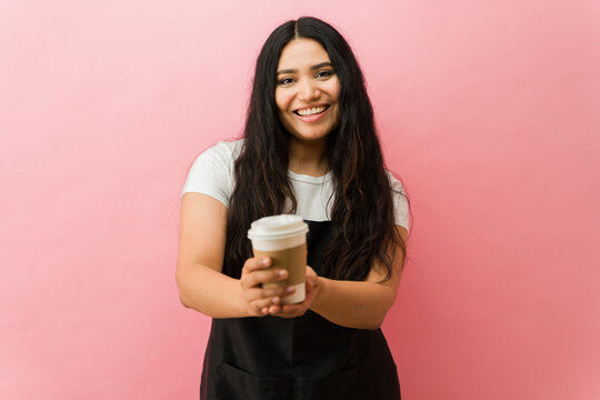 Latin woman barista offering takeaway coffee smiling cheerfully