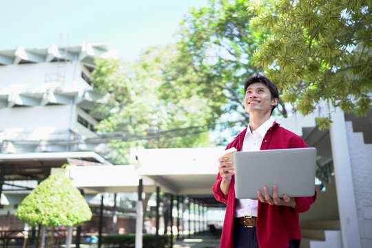 Man working remotely outdoors, drinking coffee and using laptop in city park - Powered by Adobe