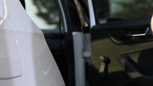 Close up view of a hand pulling the handle of a white modern car. A woman opens the door and enters the vehicle to start driving.

