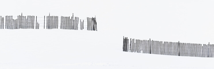 black and white silhouette of broken snow fence on snowy hillside