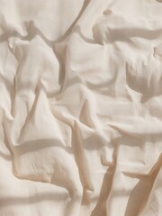 A light beige fabric with many natural wrinkles and folds. Strong sunlight creates deep shadows and a textured background.