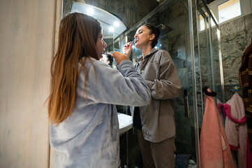 Morning routine unfolds in a cozy bathroom as a young girl brushes her teeth while her mother enjoys self-care time, creating a nurturing bonding moment before the day begins