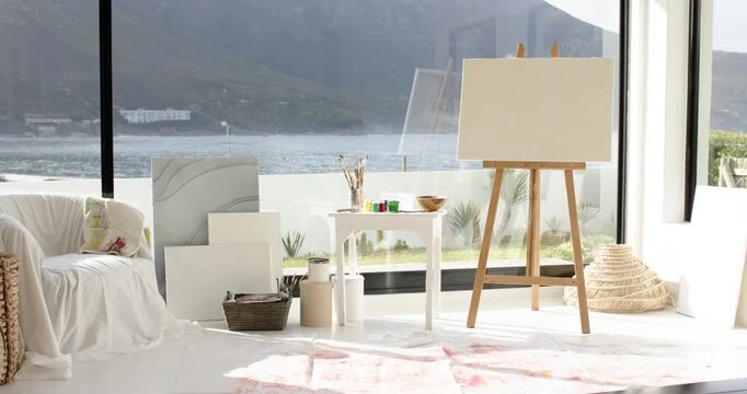 Camera holding steady view of studio corner with easel and supplies beside window overlooking lake
