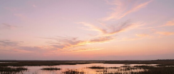 Stunning pastel sunset casts golden light over serene marshland waters at twilight
