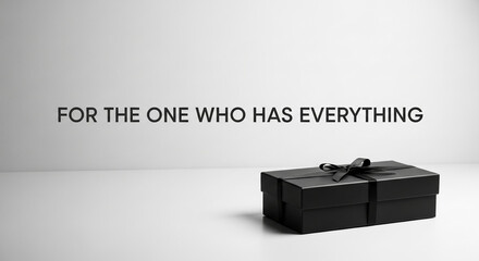 Black gift box with ribbon on surface with text "FOR THE ONE WHO HAS EVERYTHING", representing present for celebration or special occasion