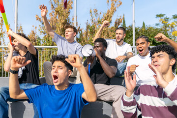 Diverse young male friends watching a game, shouting and celebrating with excitement and passion in an outdoor venue