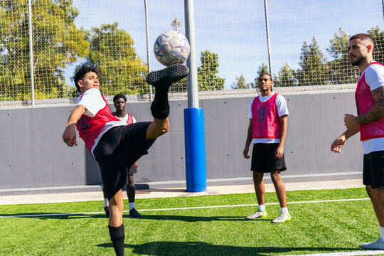 Soccer player controlling ball with his foot, practicing skills during training with teammates on a sunny field - Powered by Adobe