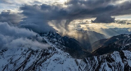Dramatic sun rays pierce stormy clouds above rugged snow covered mountain peaks at sunrise