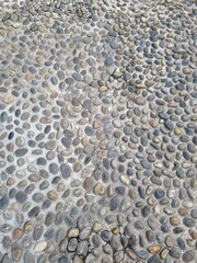 A textured background of a unique mosaic pavement made of natural, rounded stones of different colors and sizes, set in a light-colored surface on a street in Milan.
