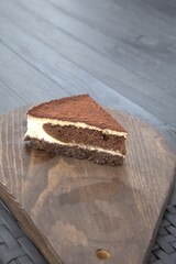 Close-up shot of a single slice of chocolate and cream cake on a wooden board. Detailed texture of the dessert with soft blurred background.