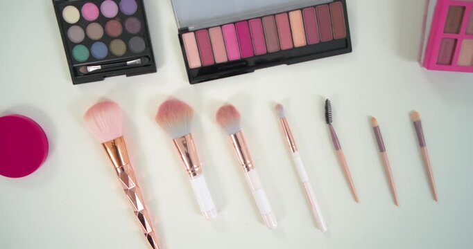 Camera pulling back panning over white table revealing brushes palettes lipsticks rings for display