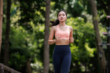 Young Asian woman wearing sports bra and leggings, running outdoors through a green park, promoting fitness and healthy lifestyle