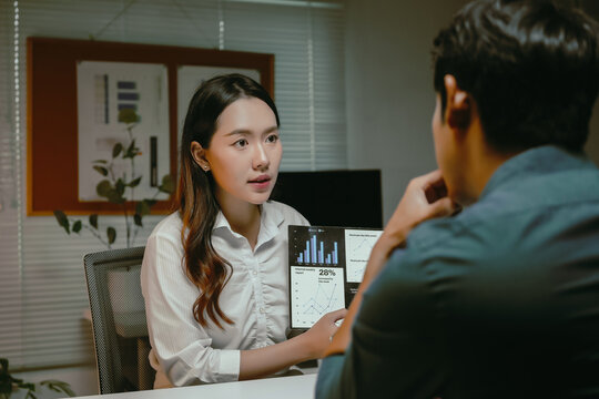 Businesswoman presenting financial data and charts on a tablet to a male colleague, discussing corporate strategy and progress