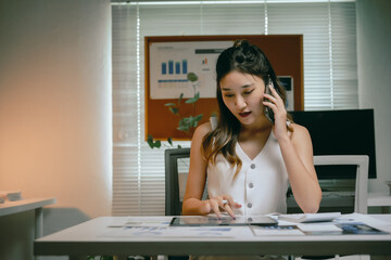 Asian businesswoman working in office, talking on phone while using a digital tablet, managing tasks and communicating