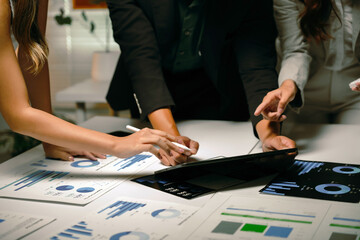 Business professionals collaborating, discussing market trends, and analyzing financial data reports and digital statistics on a tablet during a corporate meeting