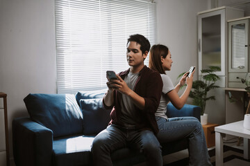 Couple sitting on a couch back to back, absorbed in their smartphones and ignoring each other at home