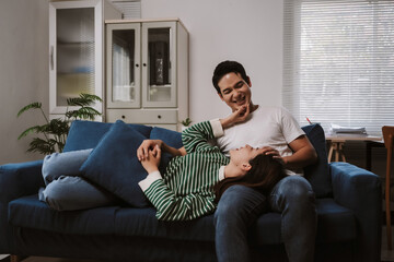 Asian couple resting and smiling on a sofa, enjoying each other's company in a comfortable home interior