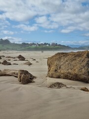 Walking people on wide beach of Biscayne bay, Spain. Surf beach with surfers and mountain on background. Active lifestyle concept. Calm picturesque seacoast. Active tourism. Peaceful day on coastline.