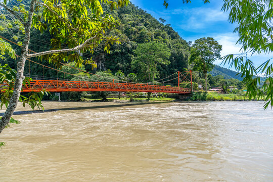 Monzon Bridge in Tingo Maria spans a tropical river with lush vegetation, mountains, and bright daylight.