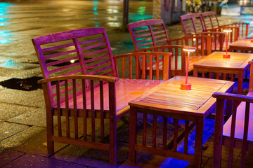 Colorful outdoor cafe seating glowing under night lights on a rainy street