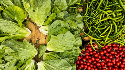Fresh green curly lettuce, long pointed green peppers, and bright red cherry tomatoes standing side by side at the market. Vibrant colors and a healthy eating theme.