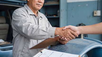 Mechanic shaking hands with customer in auto repair shop after completing car service and signing maintenance agreement on clipboard
