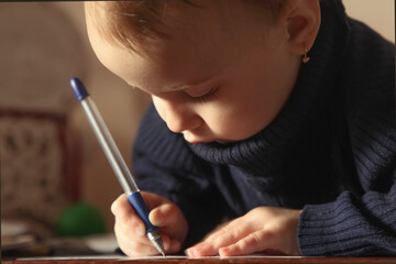 A toddler carefully learning to write with deep concentration.
