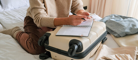 Travel planning scene with carry-on suitcase used as desk, open notebook and smartphone, hands writing a packing list in a cozy hotel room, minimalist weekend getaway prep, warm light lifestyle.