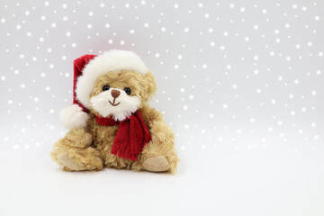 Plush teddy bear wearing a red Santa hat and scarf, isolated against a gray, snowy background. Christmas card with copy space.