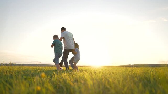 Happy team play.Group of children on grass in park. Boys and girls play with ball at sunset in park.Active team plays with ball in summer.Schoolchildren rest in nature.Children play football with ball