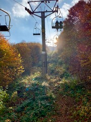 Sunlit Chairlift Ride Through Autumn Forest in the Mountains; rustic open-air chairlift rises through a glowing autumn forest in the mountains of Ukraine