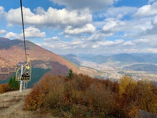 Autumn Mountain View with Chairlift in Ukraine; panoramic autumn landscape in the mountains of Ukraine featuring a yellow chairlift gliding above colorful foliage