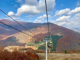 Autumn Mountain View with Chairlift in Ukraine; panoramic autumn landscape in the mountains of Ukraine featuring a yellow chairlift gliding above colorful foliage