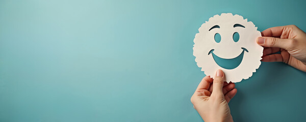 Hands hold paper smile face on blue. Positive thinking, world mental health day concept. Paper cut out face shows good mood and happiness. Happy client feedback review symbol.