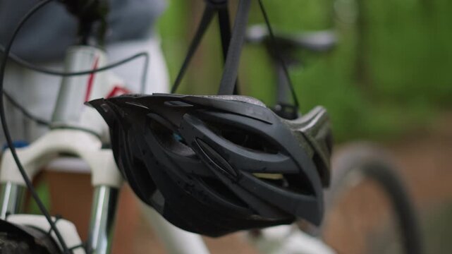 Cyclist Gear Near Trail, Helmet Hanging By Forest Trail, Postride Setting With Blurred Green Scenery Background, Quiet Atmosphere With Cyclist Gear And Helmet Beside Nature Trail In Woods