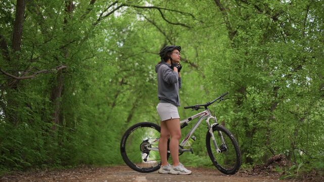 Asian Fitness Rider Making Final Adjustment Before Ride, Tightening Strap And Looking Forward Down TreeLined Track, Confident Breath And Focused Stance, Small PreRide Ritual Before Pushing Pedals