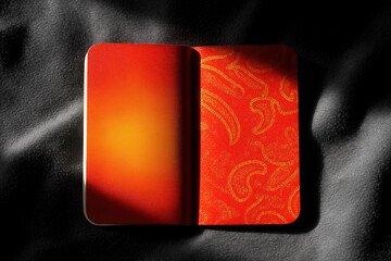 Bright red notebook placed on dark fabric surface in morning light