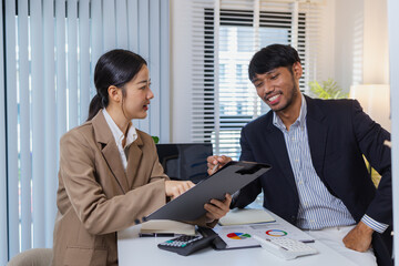Business colleagues are engaged in a collaborative discussion, analyzing financial charts and reports on the wall and table. They exchange ideas, review strategies, and plan future goals.