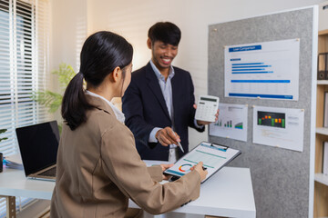 Business colleagues are engaged in a collaborative discussion, analyzing financial charts and reports on the wall and table. They exchange ideas, review strategies, and plan future goals.