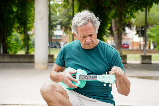 Elderly man tuning ukulele in park setting