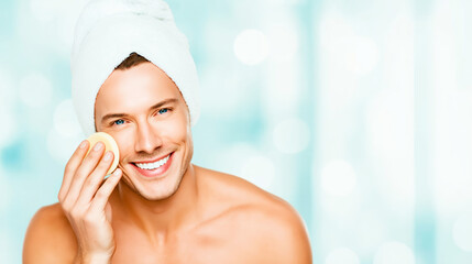 Young man applying facial foundation with makeup sponge to cheek, smiling, having fresh skin for daily beauty routine
