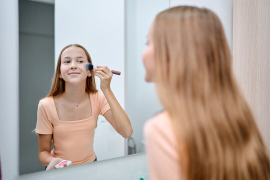 Teenager applying makeup in a bathroom mirror