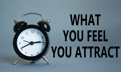 What you Feel you Attract you symbol. Wooden blocks with words What you Feel you Attract. Beautiful grey background with alarm clock. Business and What you Feel you Attract concept. Copy space.