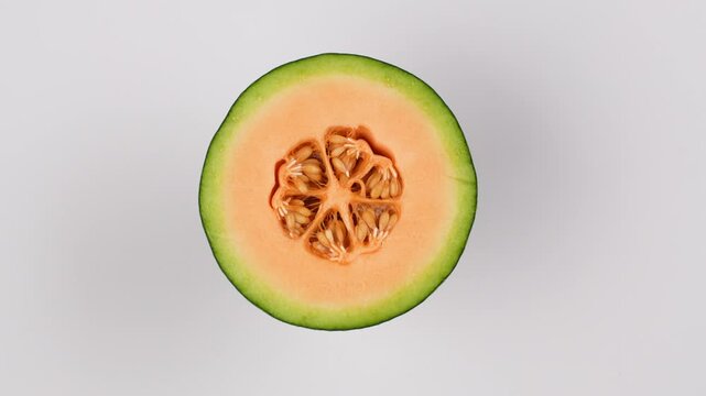 Rotating half green netted melon close-up. Fresh cantaloupe showing orange flesh and seeds. Healthy food concept.