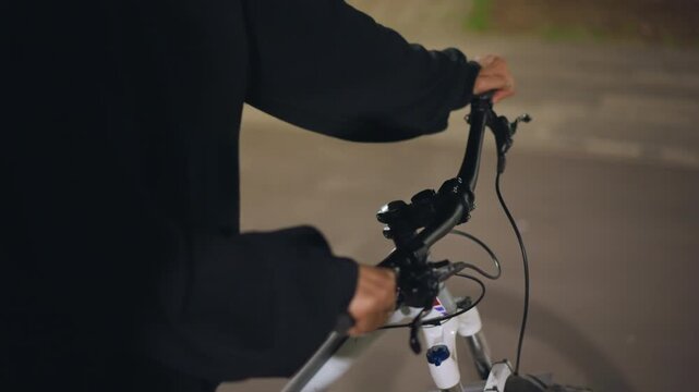 Empty Street Push Of Bicycle At Night, Person In Dark Hoodie Walks Bike Across Intersection With Subtle Motion Blur, CloseUp Of Hands On Handlebars And Steady Frame, Contemplative Nocturnal Journey