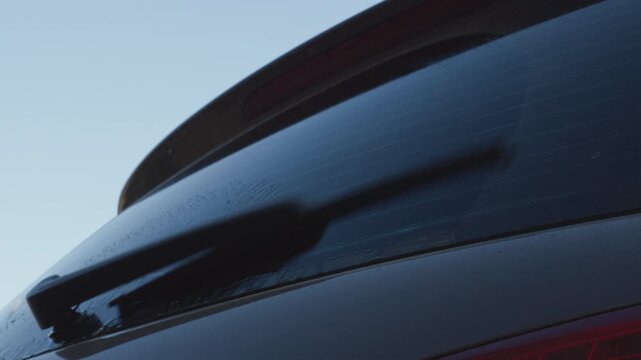 Car rear window washer spray and wiper blade cleaning wet glass with detailed mechanical sound in close up view