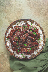 crispy beef, with green onions and sesame seeds, on a rice pad, in a bowl with chopsticks, on a textured surface, no people