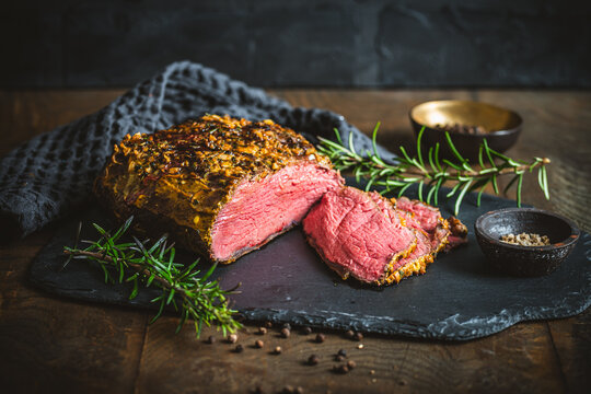 Roast beef with a mustard and herb crust, fresh from the oven, a few slices cut open, on a rustic wooden table
